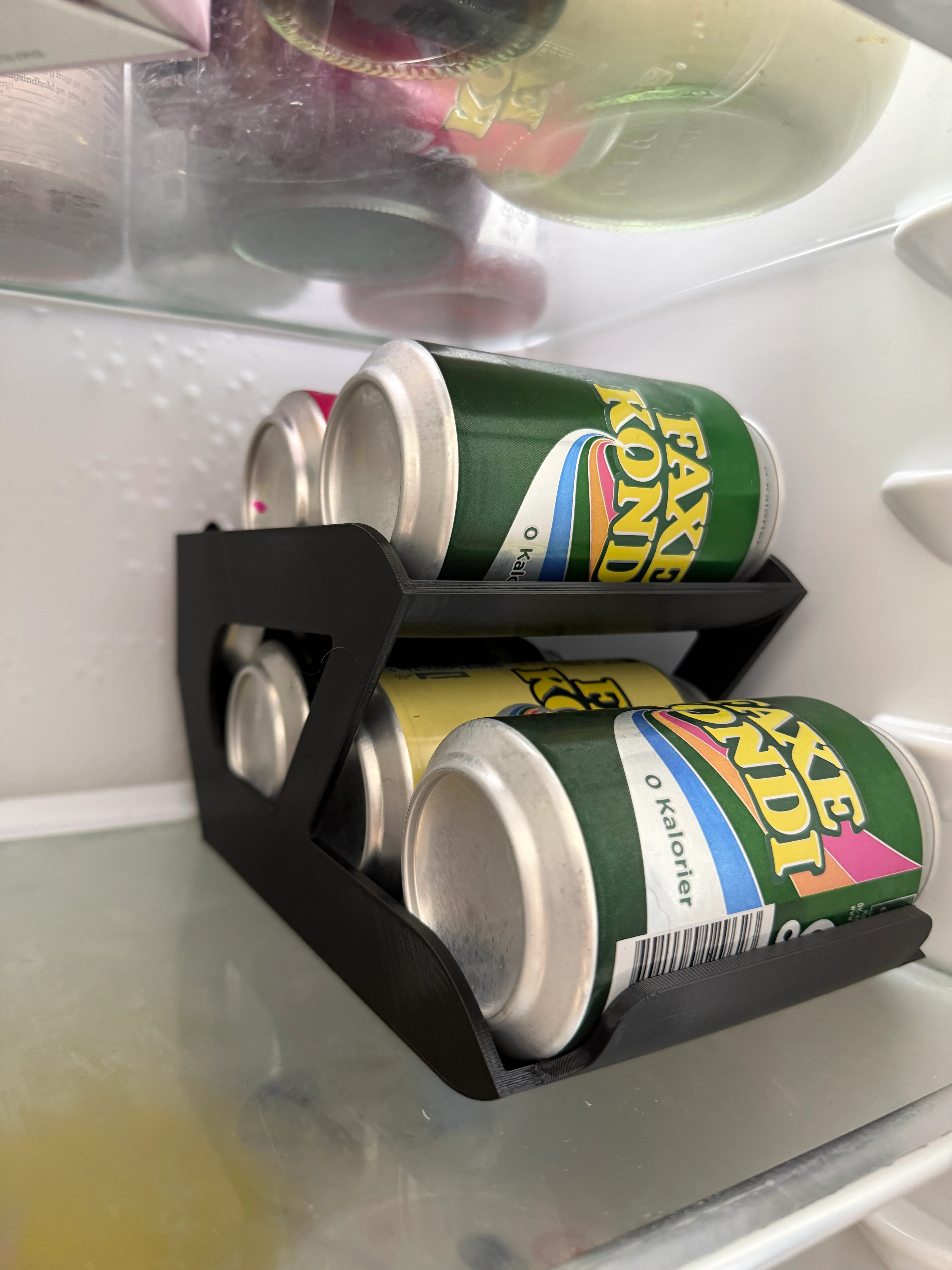 3D-printet dåsedispenser i sort, fyldt med sodavandsdåser i et køleskab